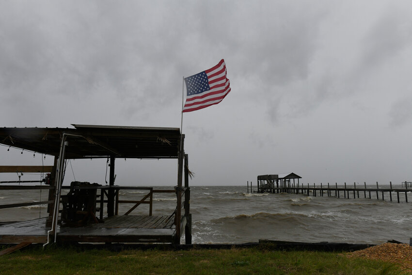 An American flag flaps in the wind generated by the effects of Isaias on an empty beach on Friday, Oct. 9, loom overhead on Friday, Oct. 9, 2026, in Mon Louis Island, Alabama.